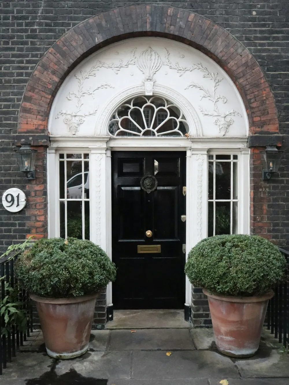 A glossy black London front door with a fanlight, flanked by clipped topiary