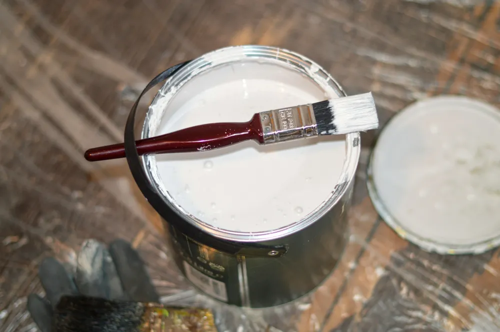 A paintbrush resting across an open tin of white paint