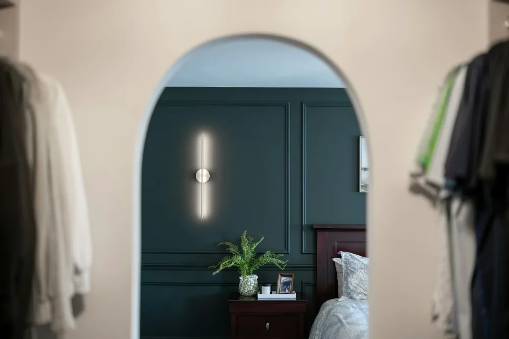 A bedroom with deep green painted wall panelling seen through an arched doorway