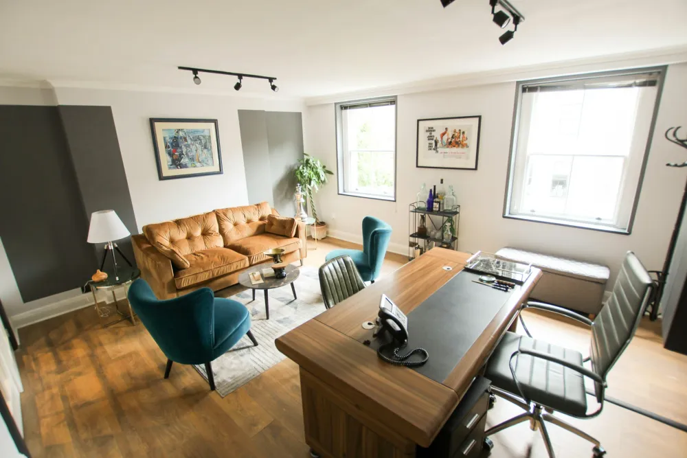 A London office with sash windows, a leather sofa and dark grey feature walls