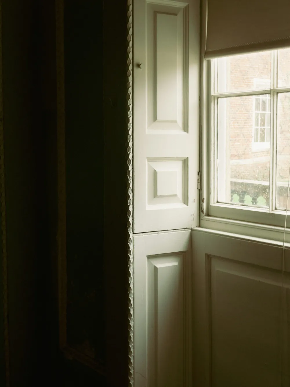 Painted timber window shutters and panelling in soft sage green, with a sash window beyond