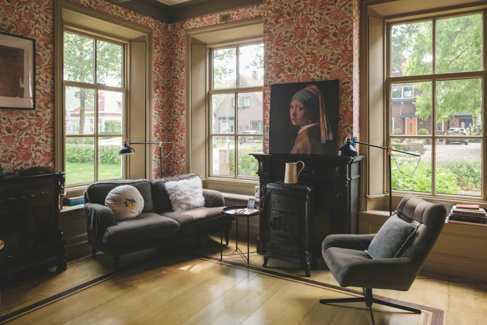A sitting room with patterned wallpaper, painted bay windows and a cast-iron stove